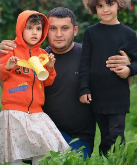 Bir babamız iki çocuğuyla birlikte yeşilliklerin arasında poz veriyor.